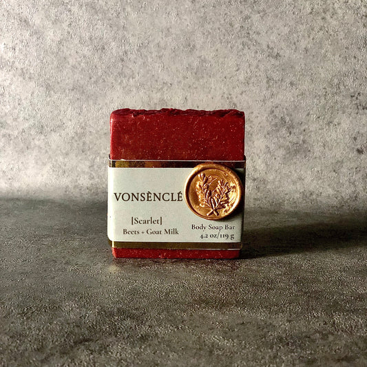 A Burgundy-red soap bar, wrapped with a grey-colored gold foil label.