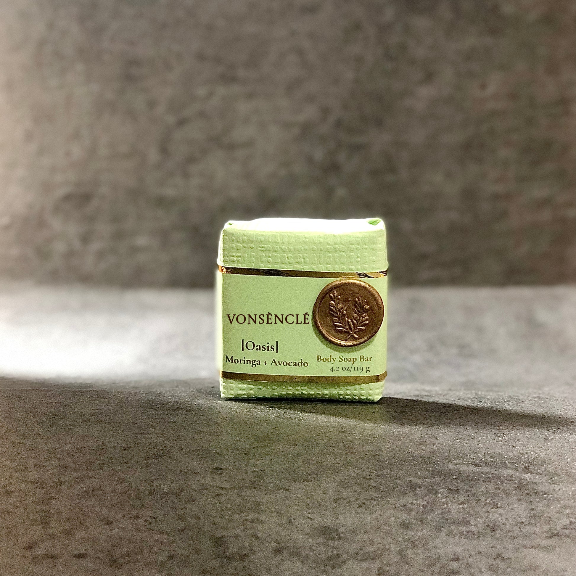 Artisanal soap bar, wrapped in a textured pastel green wrapper, stamped with a wax seal.