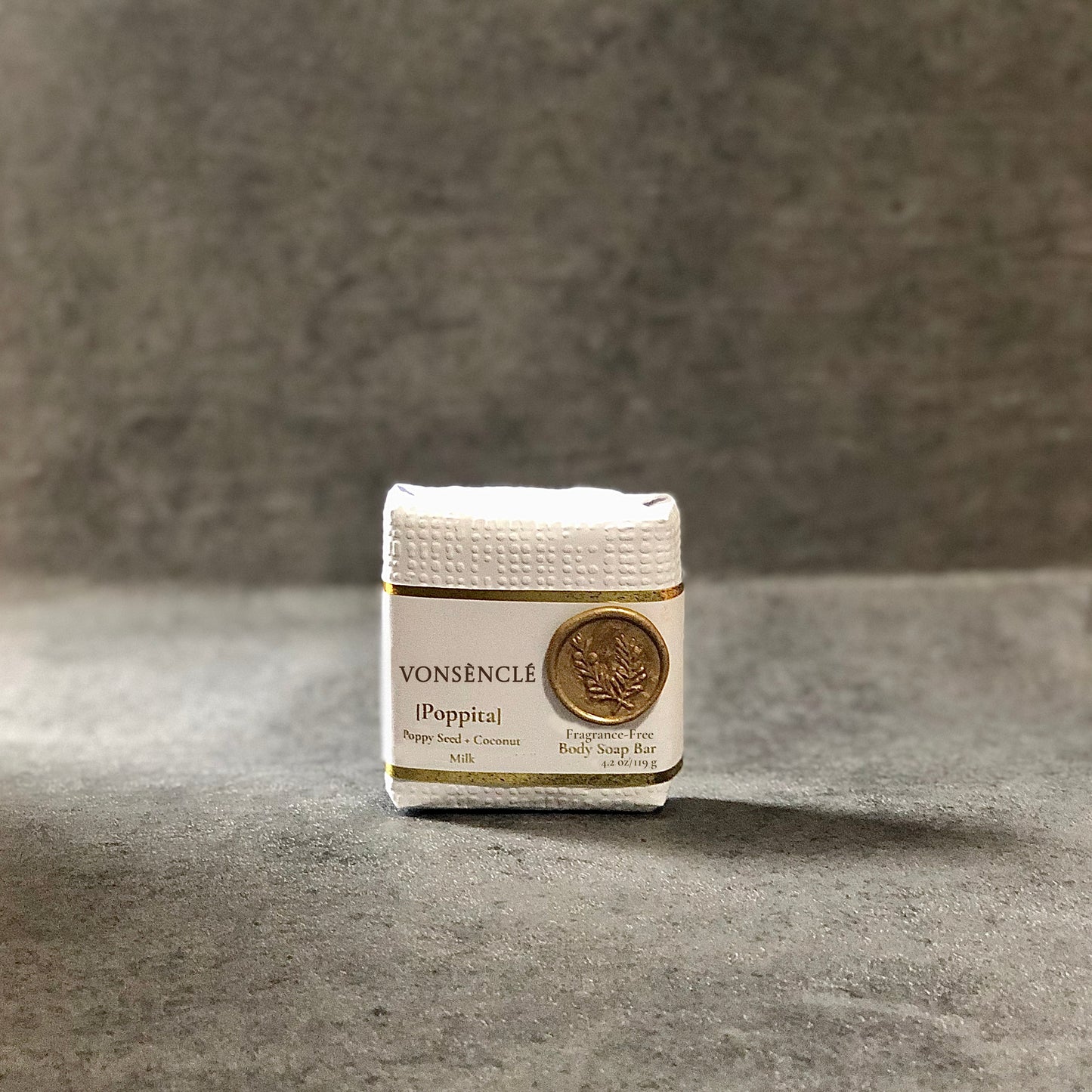 Cold process soap wrapped in a white textured paper that contains a gold-colored wax stamp