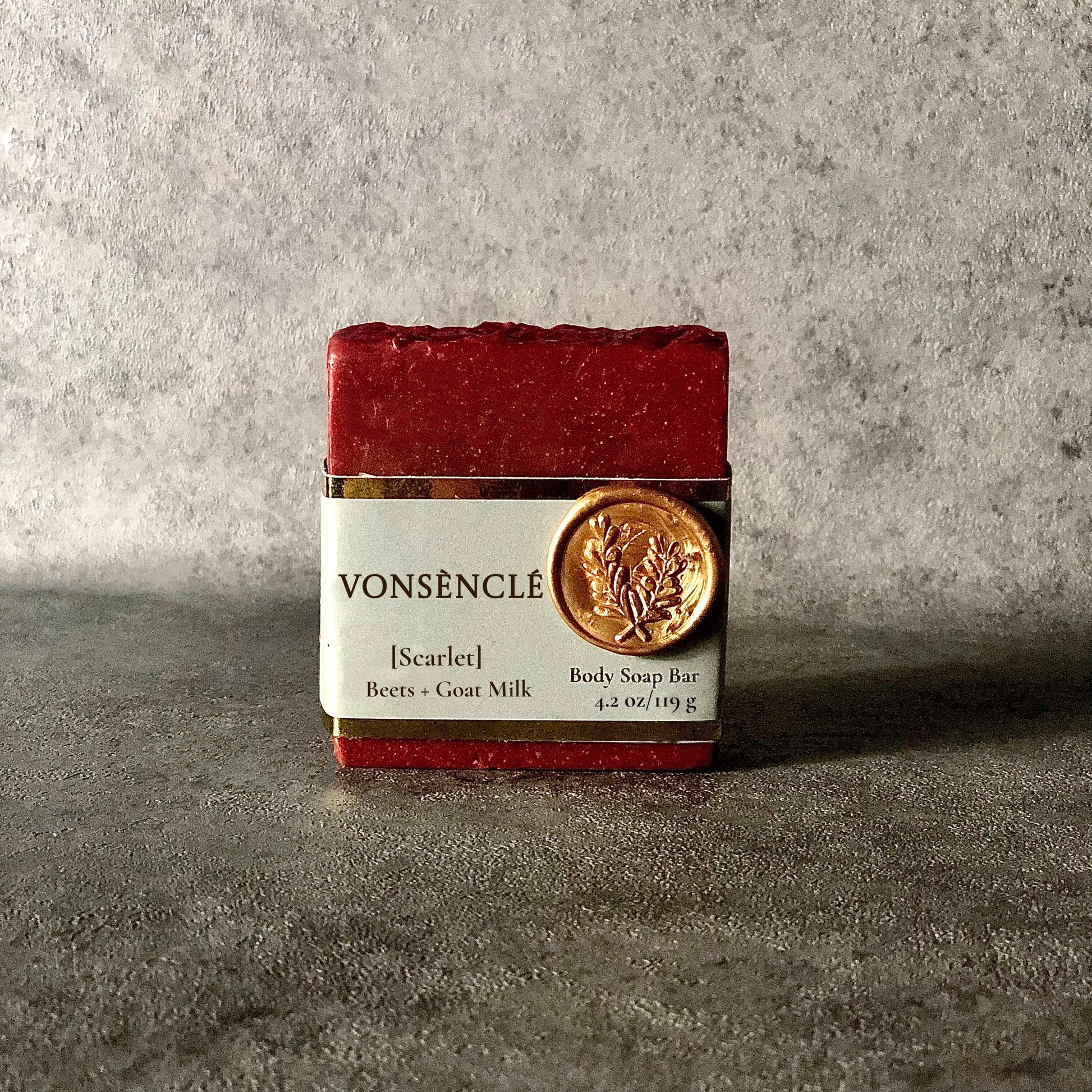 A Burgundy-red soap bar, wrapped with a grey-colored gold foil label.